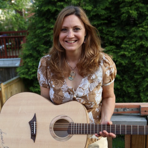 Suzanne outside in front of tree while holding a guitar